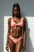 Woman wearing a pink bikini standing against a white wall with shadows.