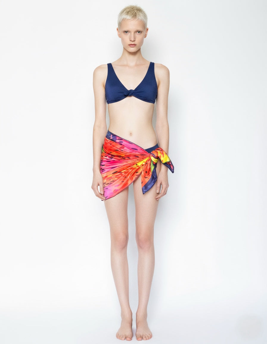 Woman wearing a navy bikini top and colorful sarong on a white background